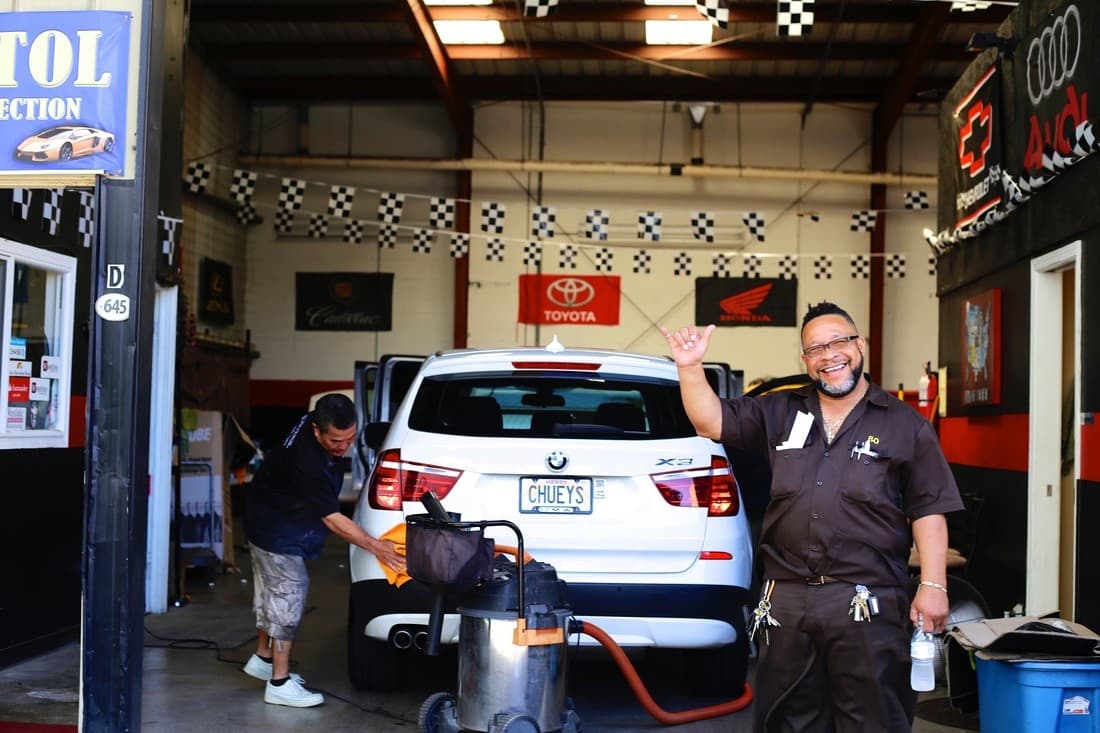 Bo Moore on the shop floor at Mark's Garage while a detailer finishes a white BMW